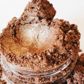 Eyeshadow makeup with brown and gold shimmer, in a clear glass container