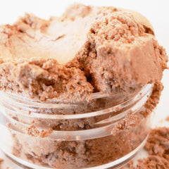 Powdered brown cosmetic product in a clear glass jar with glittery particles