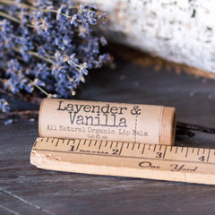 Lip balm tube with "Lavender & Vanilla" text, brown paper, and wooden ruler on dark surface