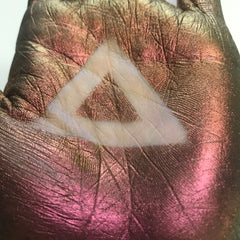 Hand with metallic bronze and pink paint, white triangle shape, showing texture and detail