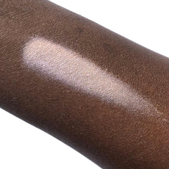 Highlighter swatch on dark skin, light pearlescent color, smooth texture, angled application