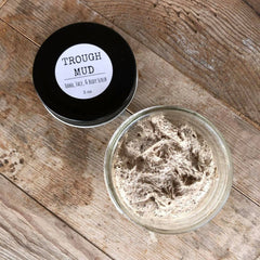Mud scrub in a glass jar, black lid with "TROUGH MUD" label, on a wooden surface