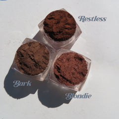 Hand applying matte brown mineral eyeshadow with a brush, showcasing loose pigment texture and blendability.