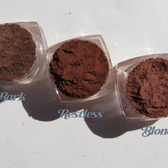 Close-up of six matte brown loose mineral eyeshadows in vegan-friendly jars with sifter lids, showcasing earthy tones.