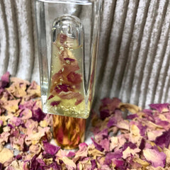 Clear glass bottle with yellow liquid, rose petals, and gold flakes, on a bed of petals