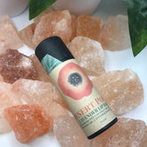 Lip balm tube with Desert Poppy label, black cap, and pink floral design on a bed of orange crystals