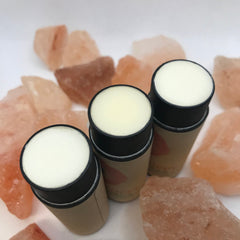 Lip balm sticks with white balm, black rim, and tan paper tube, on pink rocks
