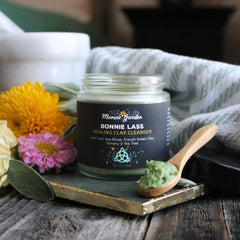 Healing clay cleanser jar with black label, green contents, and wooden spoon on a decorative tray