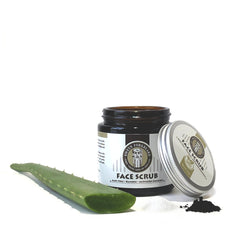 Face scrub jar with dark glass, silver lid, and green aloe vera leaf next to it