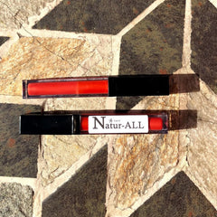 Lip gloss tubes with red gloss, black caps, and Natur-ALL branding on stone surface