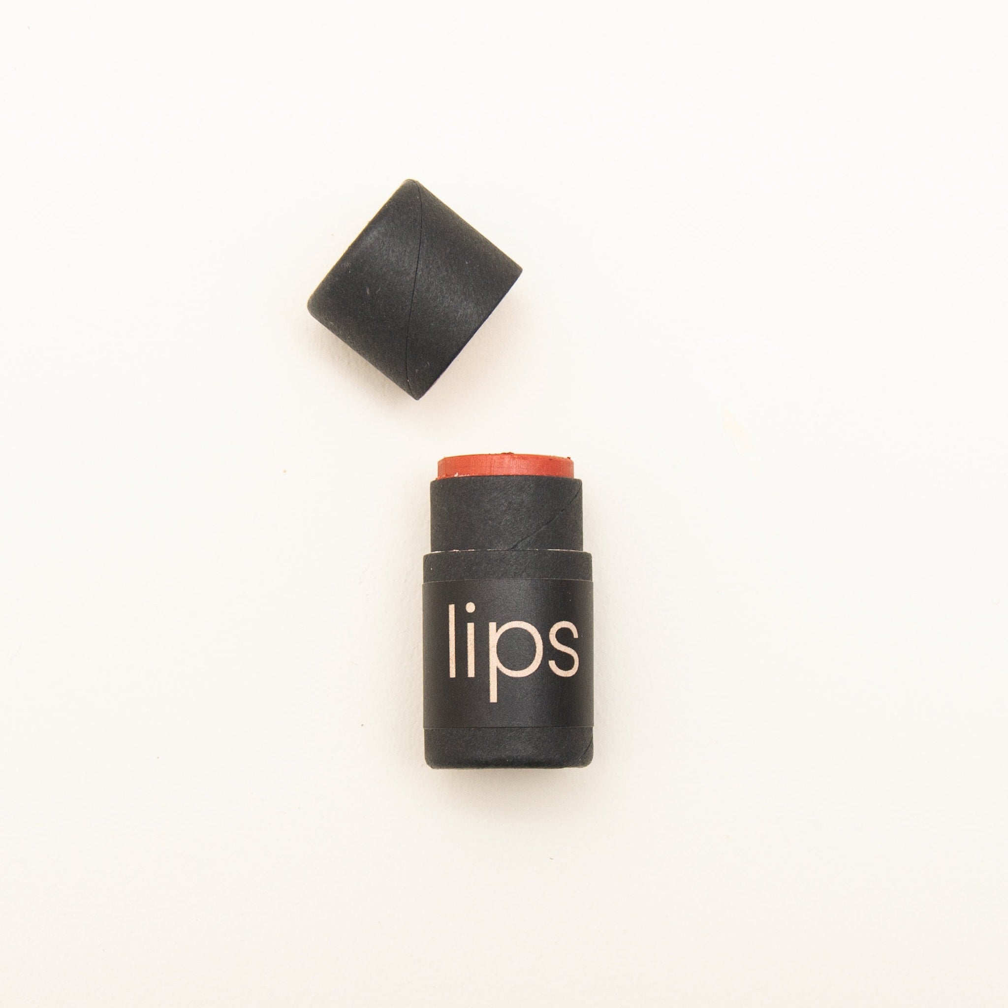 Tinted lip balm, black paper tube with coral balm, "lips" text visible