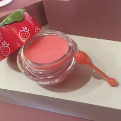 Lip balm pot with pink balm, clear glass, and orange honey stick for application