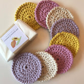 Crochet face scrubbies in yellow, pink, and purple, arranged in a circle, with soap bar