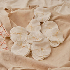 Reusable cotton pads, white circular pads, tied with gold string, on beige fabric