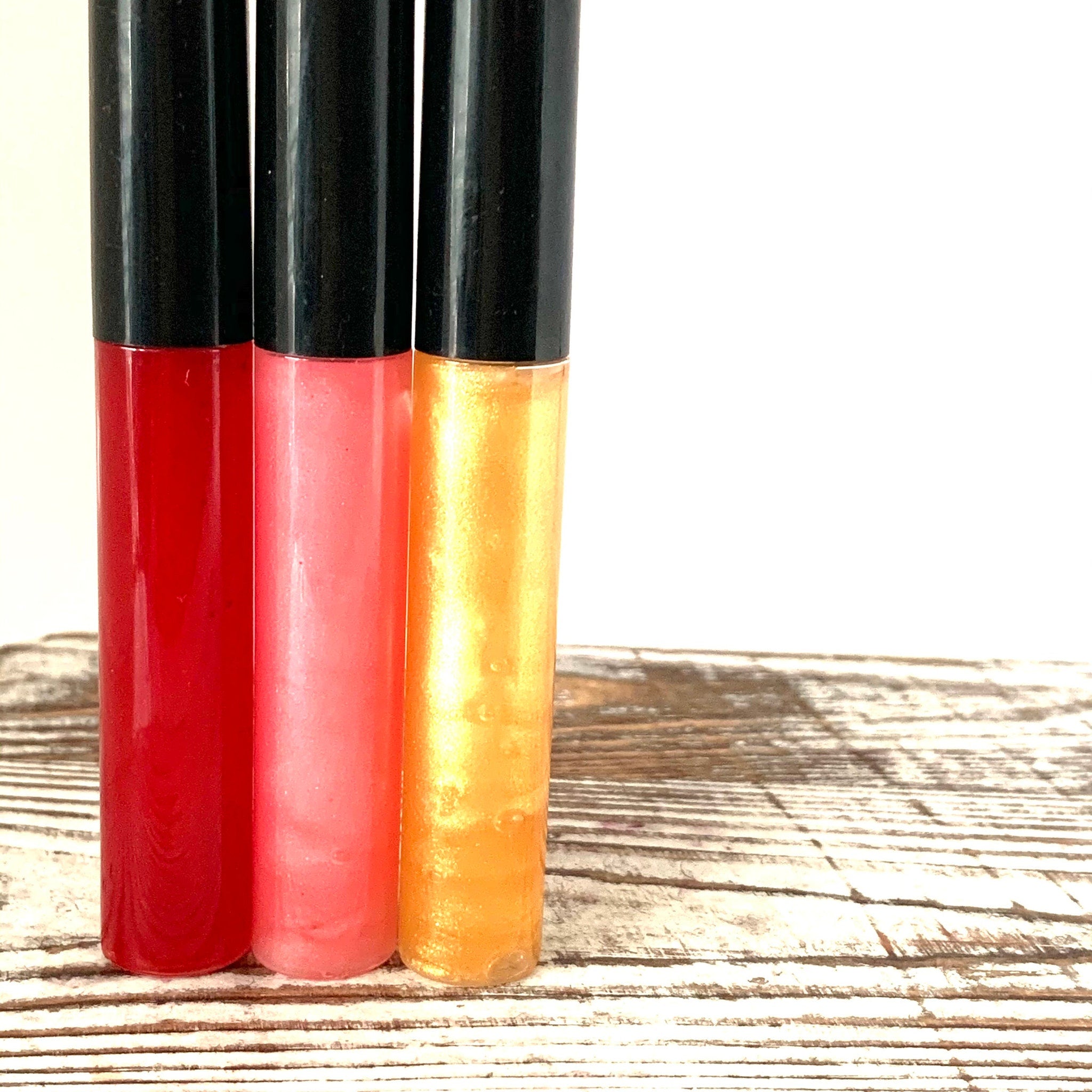 Lip gloss tubes in red, pink, and yellow with black caps on wood surface
