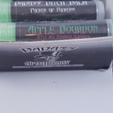 Lip balm tubes with green, black, and white text, "APPLE BOURBON" and "BADASS APOTHECARY" visible