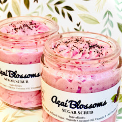 Sugar scrub in glass jars, pink with dark seeds, "Açaí Blossoms" label visible, floral background