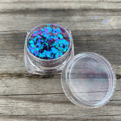 Close-up of VENUS multichrome eye shadow flakes shimmering with shifting iridescent hues in a sleek black container