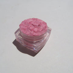 Pink powder eyeshadow in clear plastic jar with glitter details on white surface