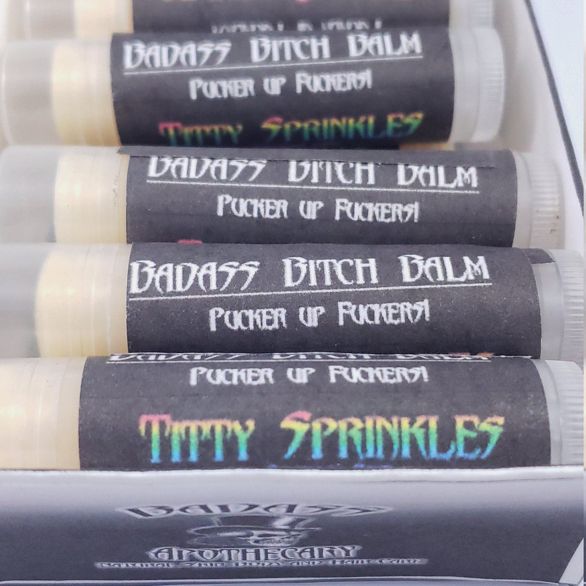 Lip balm tubes with black labels, white text, and clear plastic, Badass Apothecary brand