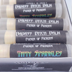 Lip balm tubes with black labels, white text, and clear plastic, Badass Apothecary brand