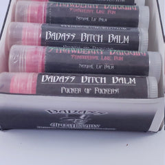 Lip balm tubes with pink balm, black labels, and clear caps, "BADASS BITCH BALM" text visible