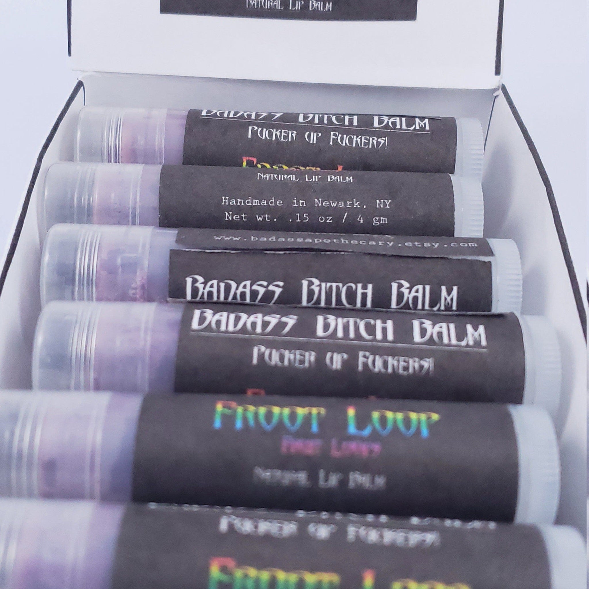 Lip balms in clear tubes with black labels, Badass Apothecary text visible, packaged in box