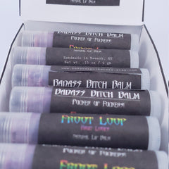 Lip balms in clear tubes with black labels, Badass Apothecary text visible, packaged in box