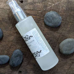 Spray bottle with clear glass, silver pump, and Ageless Botanicals label on wood surface