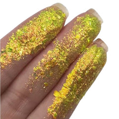 Green and gold glitter flakes on fingers, for cosmetic application