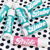 Lip balms with teal and pink labels, white tubes, and "Babe" and "Bride" text on polka dot background