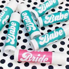 Lip balms with teal and pink labels, white tubes, and "Babe" and "Bride" text on polka dot background