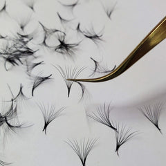 Eyelash extensions with black synthetic fibers and gold tweezers on white background
