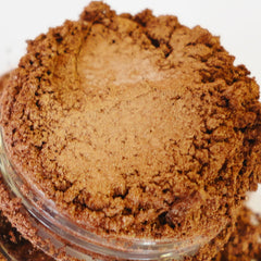Brown eyeshadow powder with metallic shimmer in a clear glass container