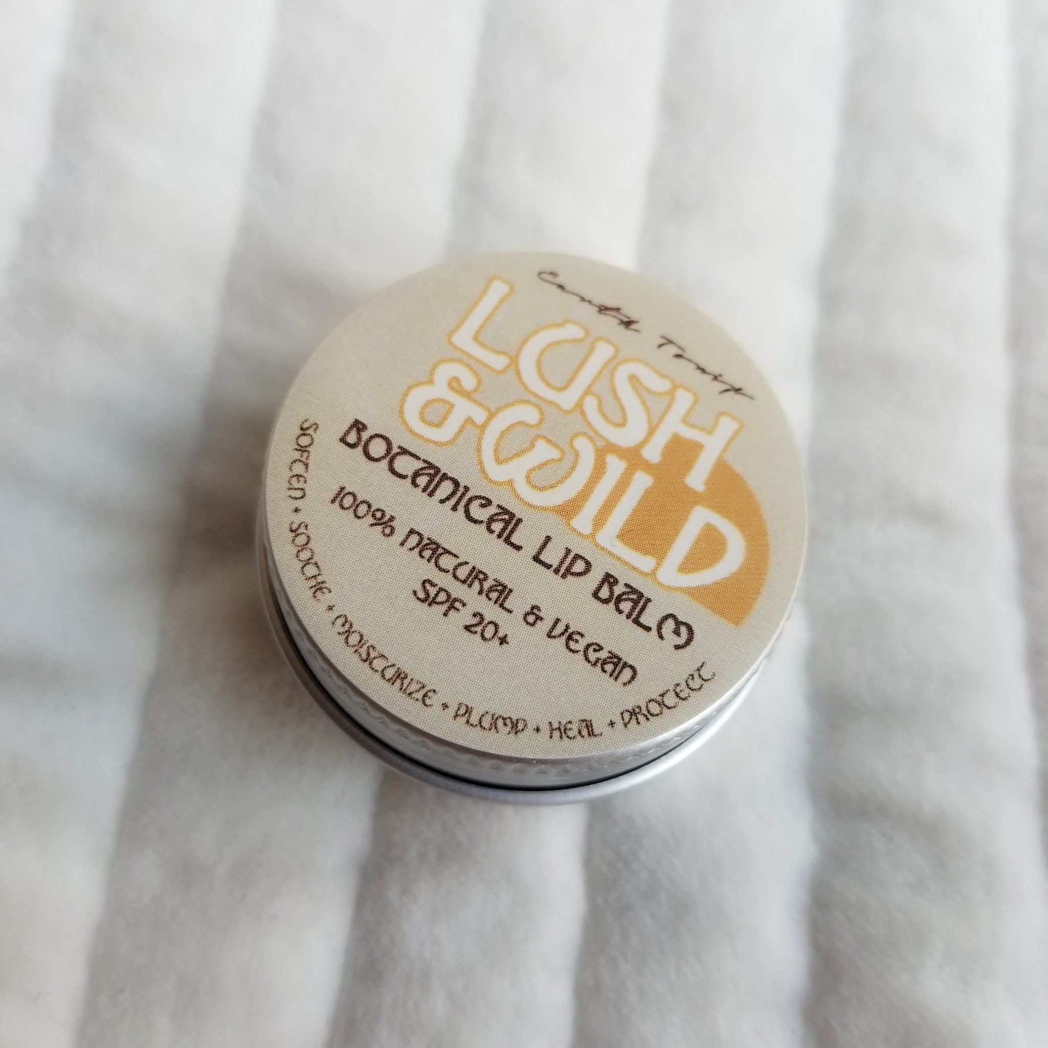 Lip balm tin with beige and gold label, silver rim, Lush & Wild text