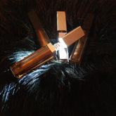 Lip gloss tubes with bronze color, silver caps, arranged on dark textured surface