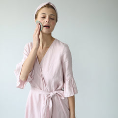 Reusable facial pad with teal trim, being used on face, with woman in pink robe and headband
