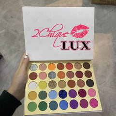 Eyeshadow palette with multiple colors, glitter, and "2Chique LUX" text on white lid