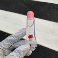 Lip gloss tube with pink cap, clear tube, and Cherry text label, held by gloved hand