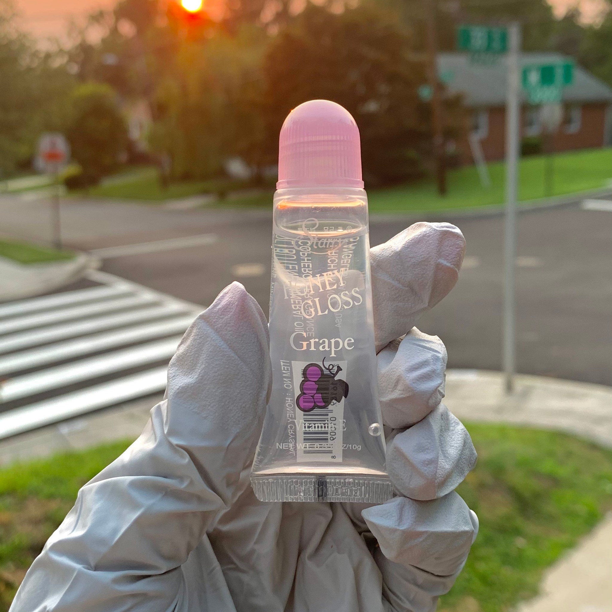 Lip gloss clear tube with pink cap held in gloved hand, Kai Kosmetics Honey Gloss Grape