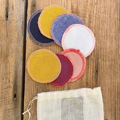 Reusable makeup remover pads in various colors with stitched edges and mesh storage bag