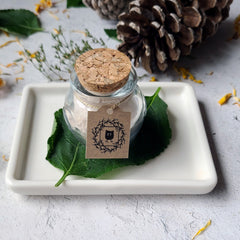 Face powder in glass jar with cork lid and tag, on white tray with leaf