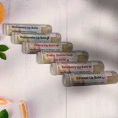 Lip balm tubes in white, clear, and blue text, on a white wood surface with fruit
