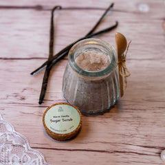 Sugar scrub in glass jar with wooden spoon and vanilla beans on wood surface, DalaNaturalBeauty label
