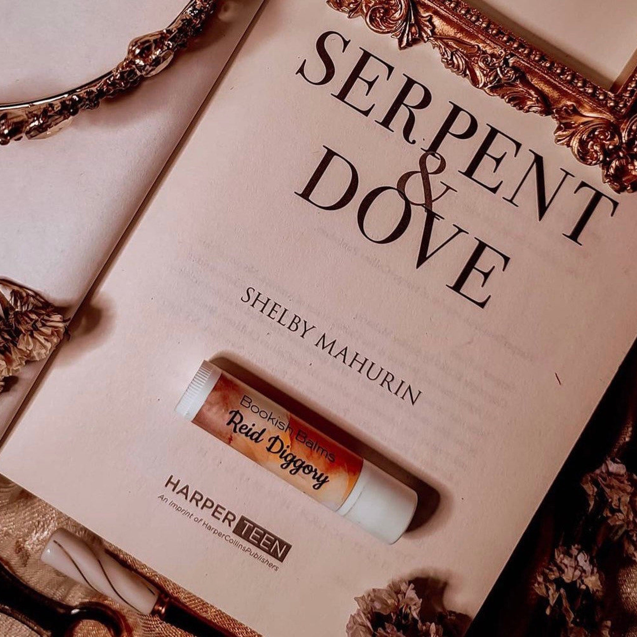 Lip balm tube with white and orange label, resting on a book, Serpent & Dove brand