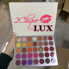 Eyeshadow palette with glittery white cover and colorful eyeshadows, "2 Chique LUX" text visible