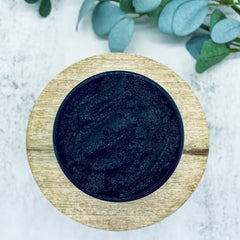 Black cosmetic product in a dark blue jar on a wooden surface, top view with green leaves