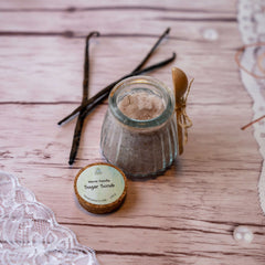 Sugar scrub in glass jar with wooden spoon and vanilla beans on wood surface