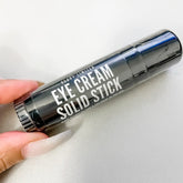 Eye cream solid stick, black cylindrical tube, white text, held by hand