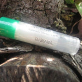 Banana lip balm with green cap, clear tube, and "BANANA" text on wood background